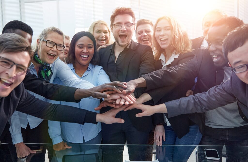 A group of workers stand together in a circle with their hands stacked